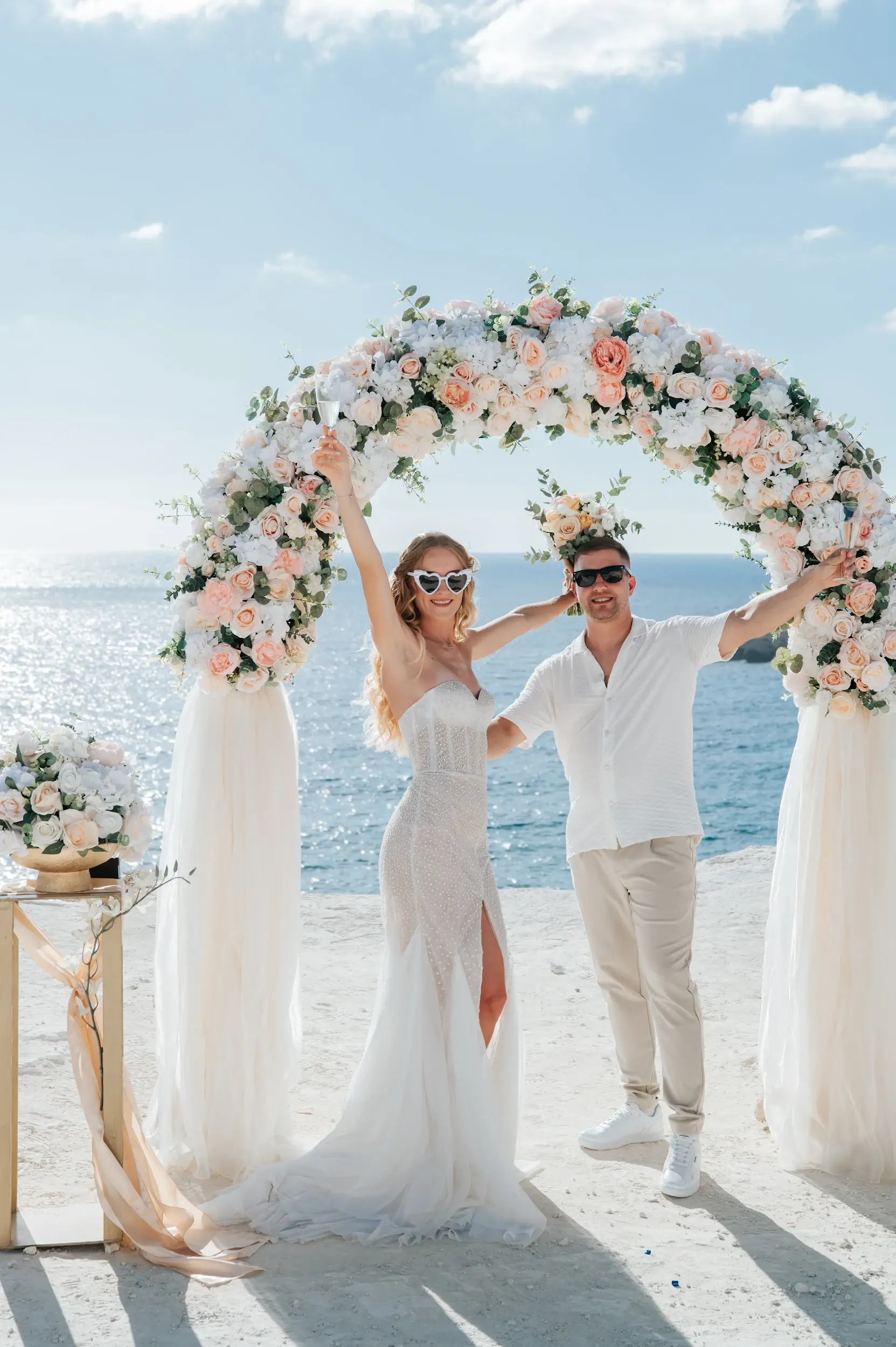 זוג נשוי חוגג תחת קשת פרחים מול הים בטקס חתונה שמח בקפריסין לזוג מישראל