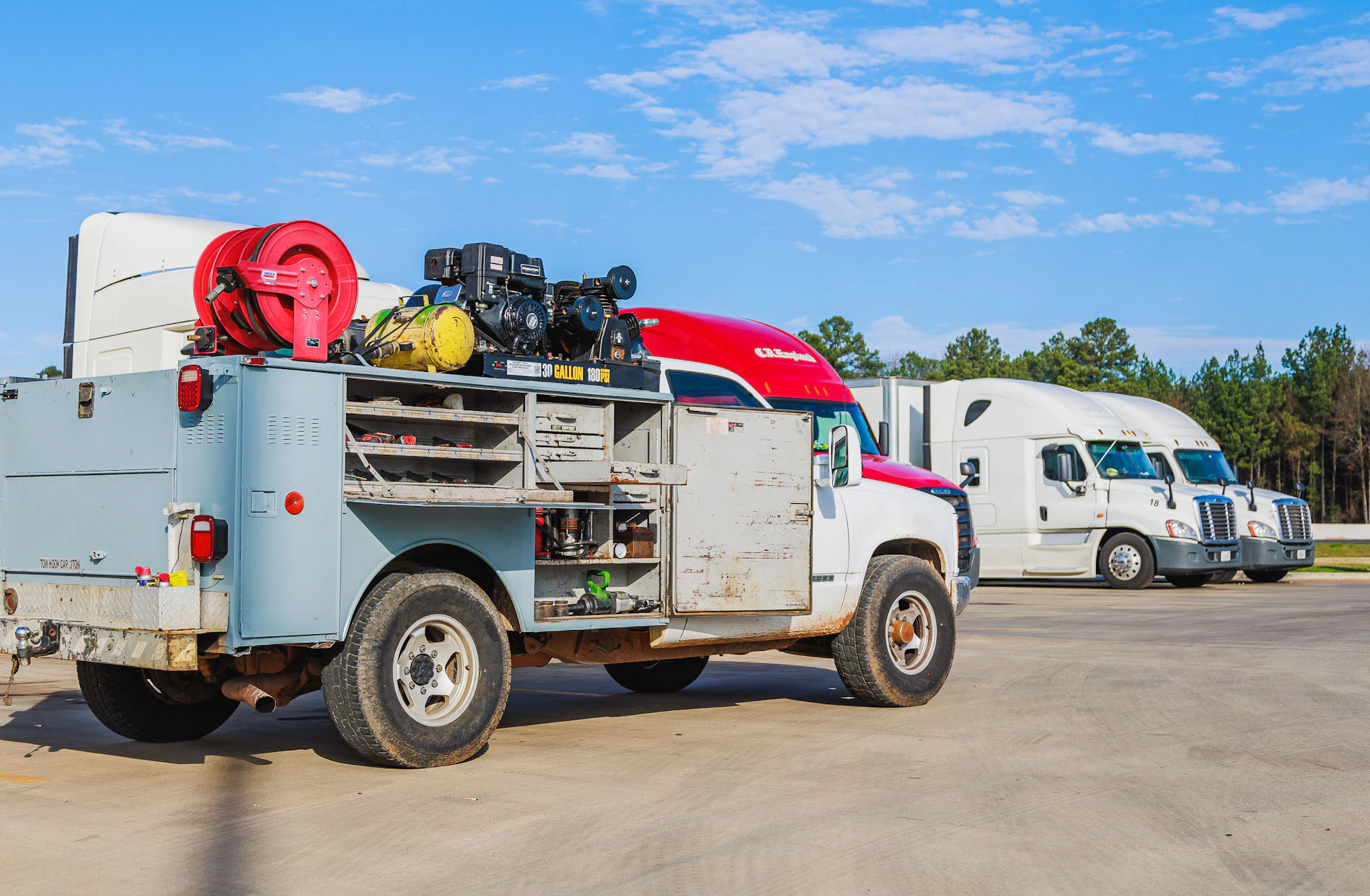Mobile truck repair vehicle with several doors open showcasing tools and equipment in a parking lot full of semi trucks 
