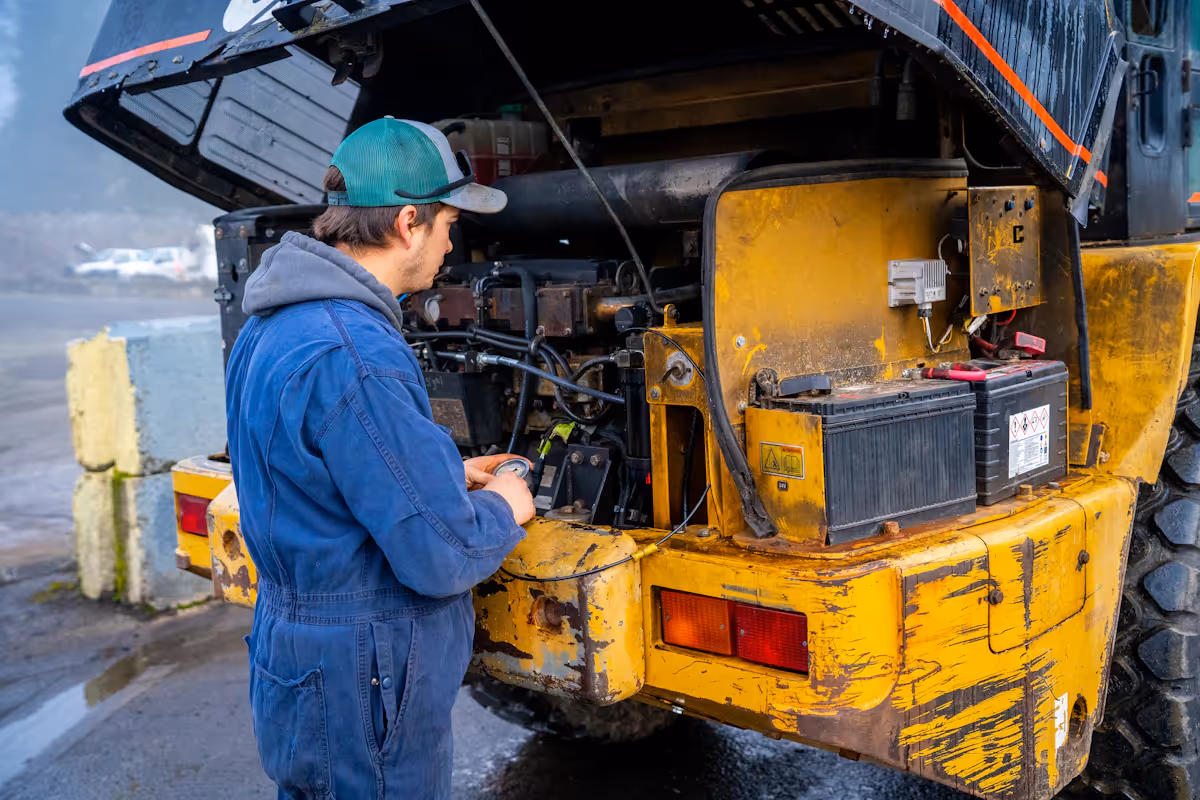 A heavy equipment technician doing maintenance on a yellow vehicle 