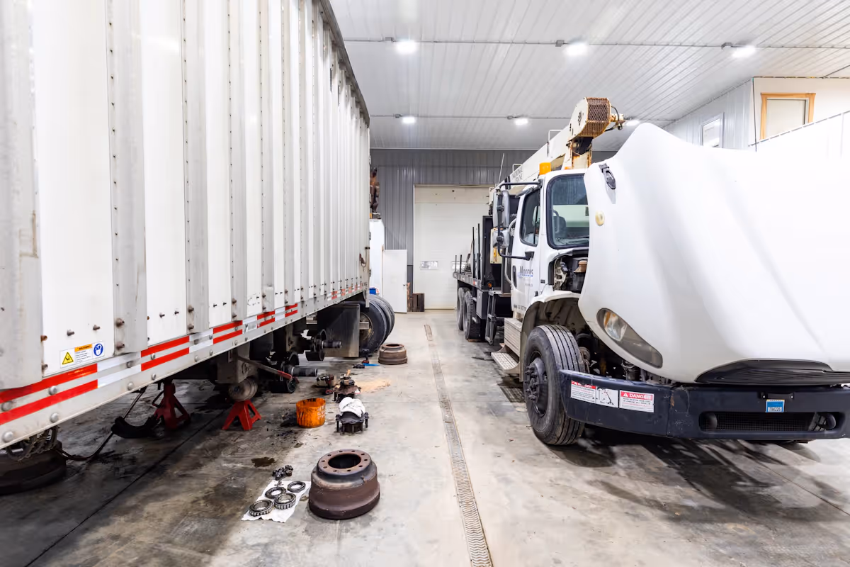 Two white trucks trailers in a garage with one having its engine hood inspected