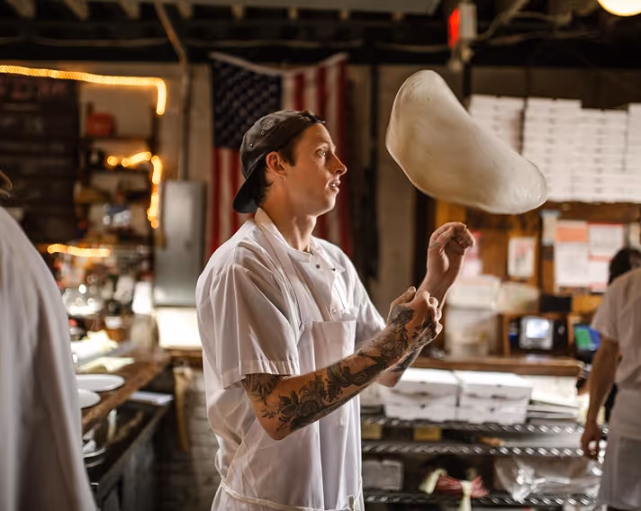 A chef tossing pizza dough in the kitchen of Roberta’s Pizza restaurant.