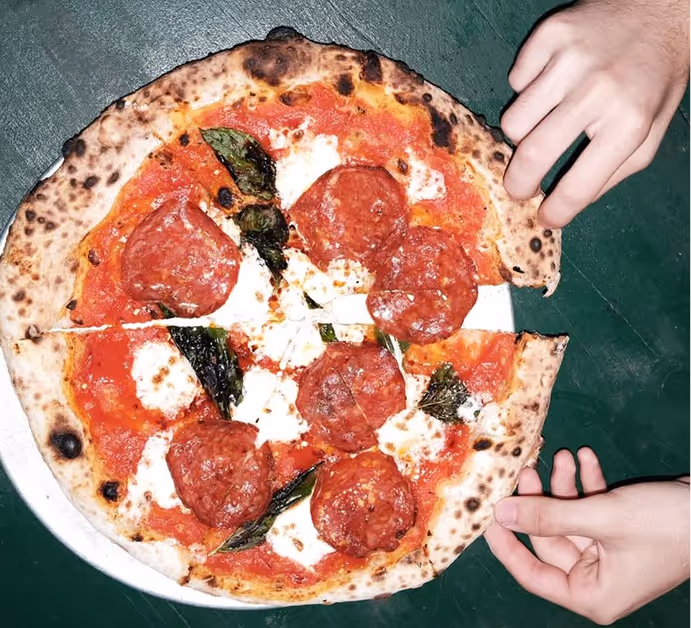 Close-up of a pepperoni and basil pizza being served at Roberta’s Pizza restaurant.