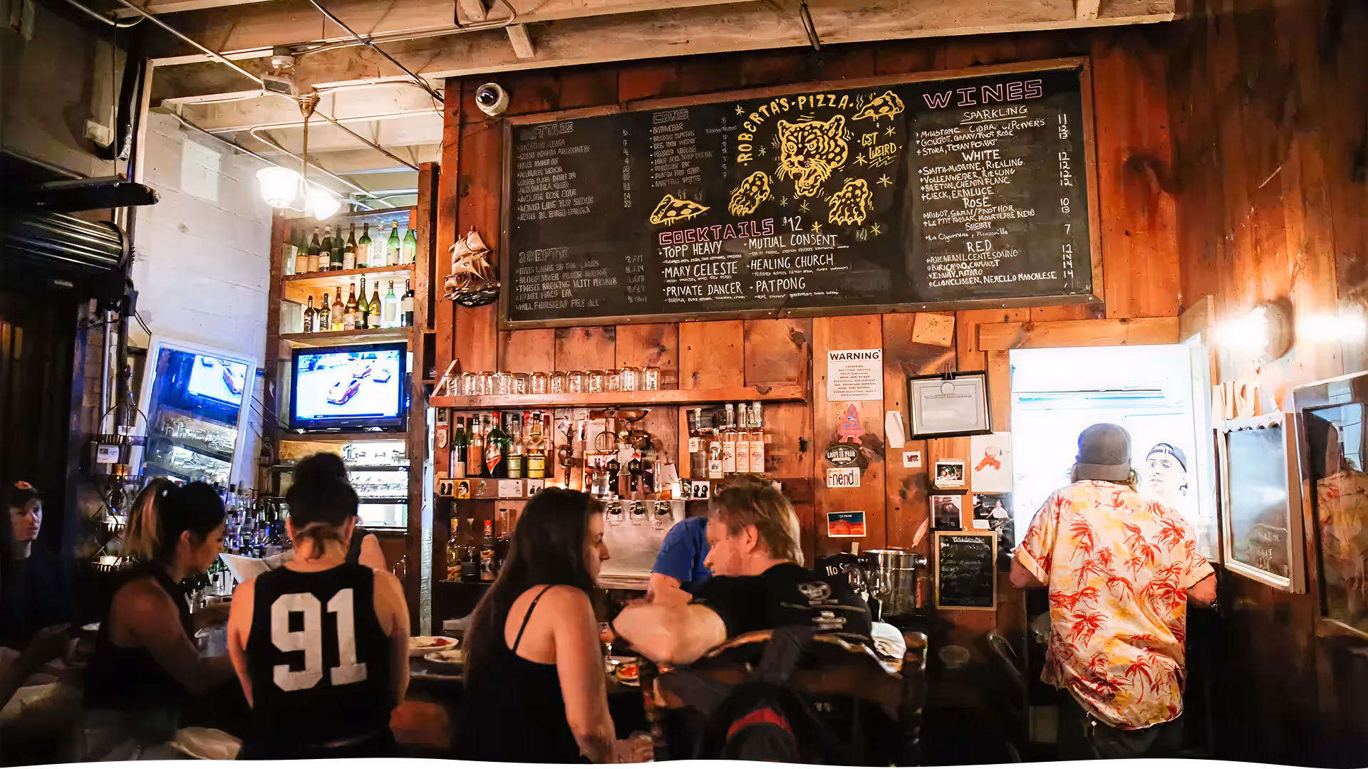 Rustic interior of Roberta’s Pizza restaurant showing the wooden bar area, chalkboard drink menu, and casual atmosphere.