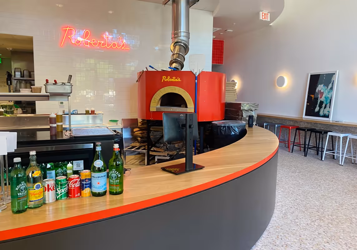 Red wood-fired oven at Roberta’s Pizza restaurant with a modern counter.