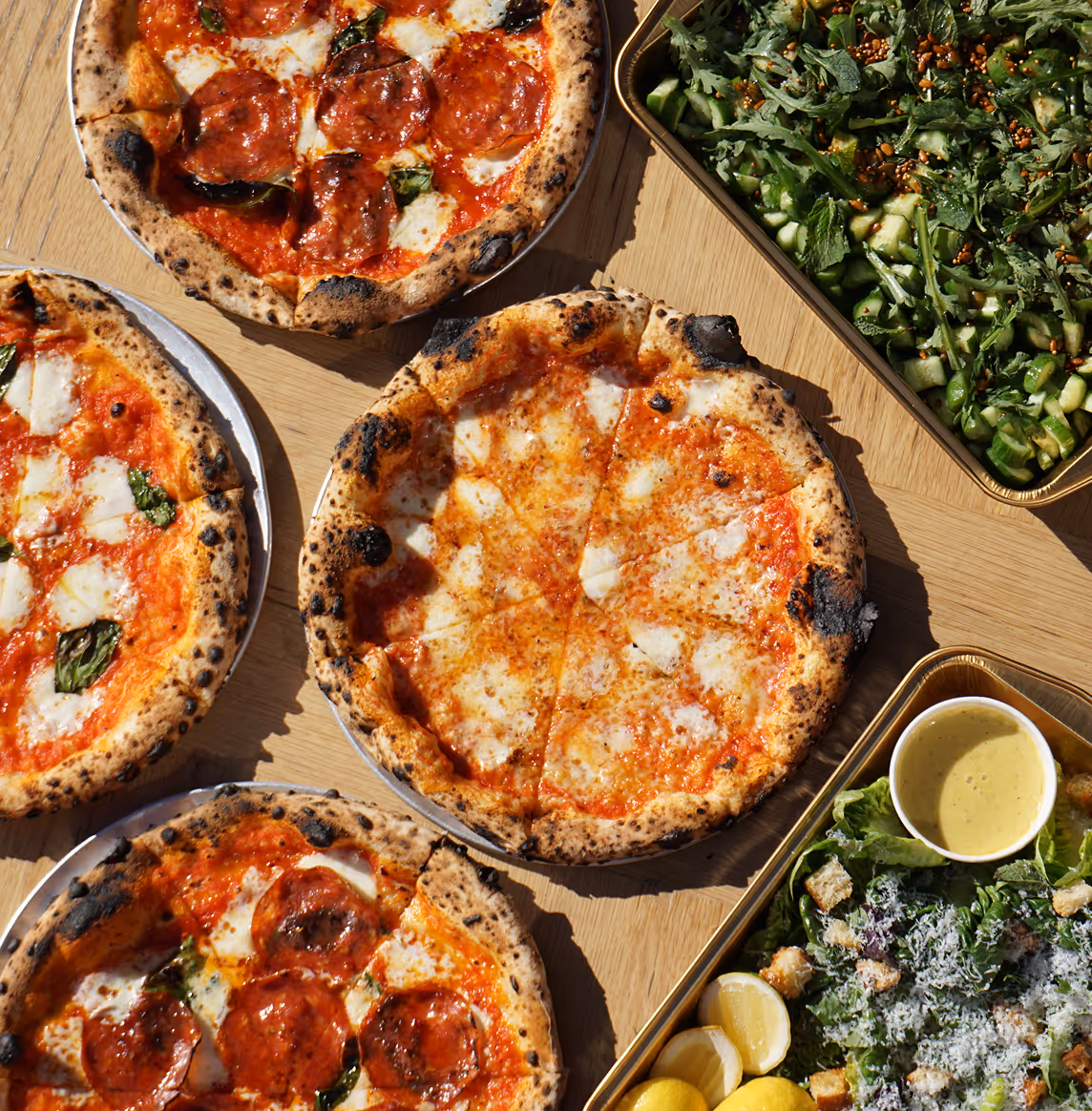 Neapolitan-style pepperoni and margherita pizzas with green salads served outdoors at Roberta’s Pizza restaurant.