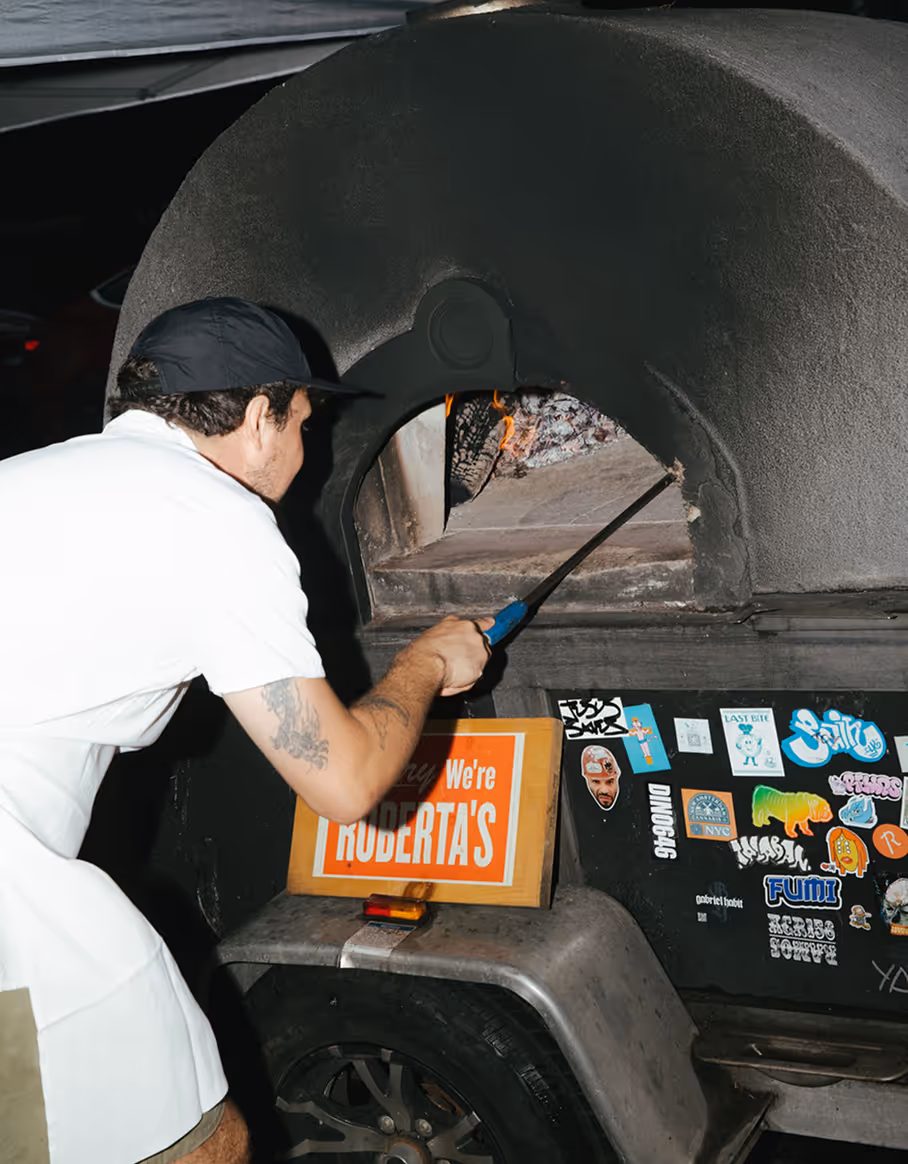 A chef using a pizza peel to cook authentic pizzas in a traditional wood-fired oven at Roberta’s Pizza restaurant.