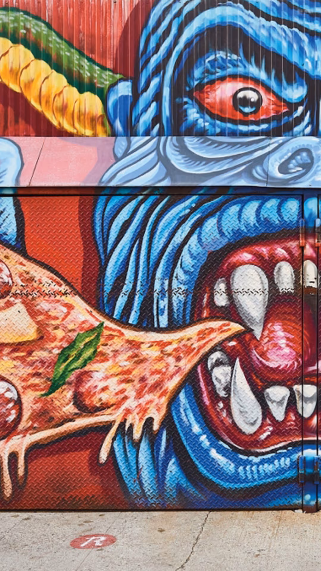 Colorful graffiti-style mural at Roberta’s Pizza restaurant featuring a blue monster eating a pizza slice.