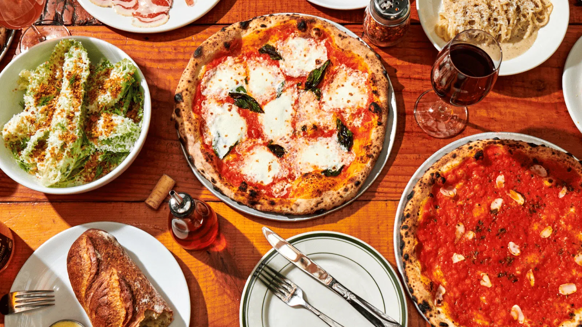 Overhead view of a table at Roberta’s Pizza restaurant with wood-fired pizzas, appetizers, and wine.
