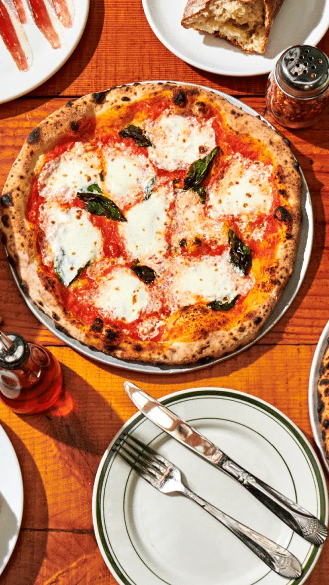 Overhead view of a table at Roberta’s Pizza restaurant with wood-fired pizzas, appetizers, and wine.