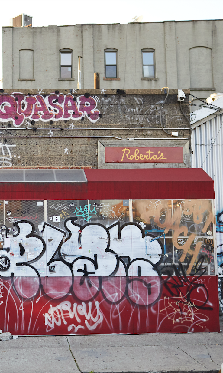 Exterior of Roberta’s Pizza restaurant in Brooklyn featuring vibrant graffiti murals and red neon signage.