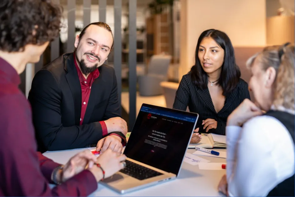 Drei Personen im Strategiegespräch am Besprechungstisch mit Laptop und Notizen