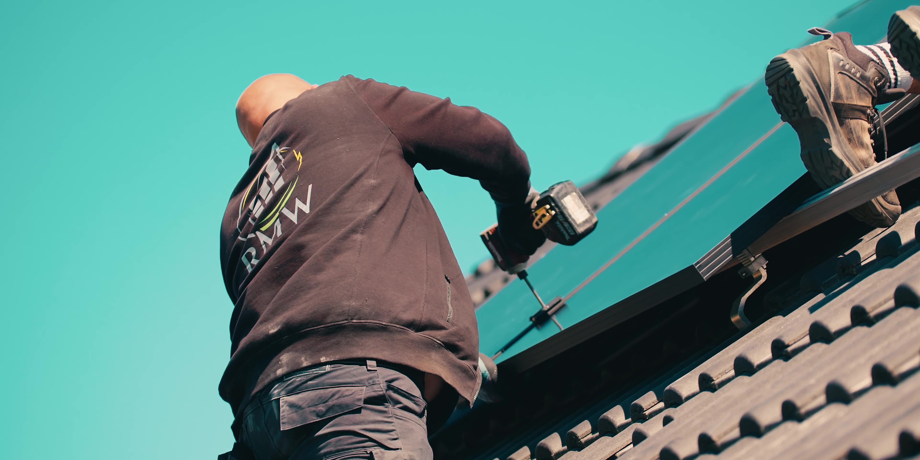 Handwerker bohrt bei der Montage von Solarmodulen auf einem Dach.