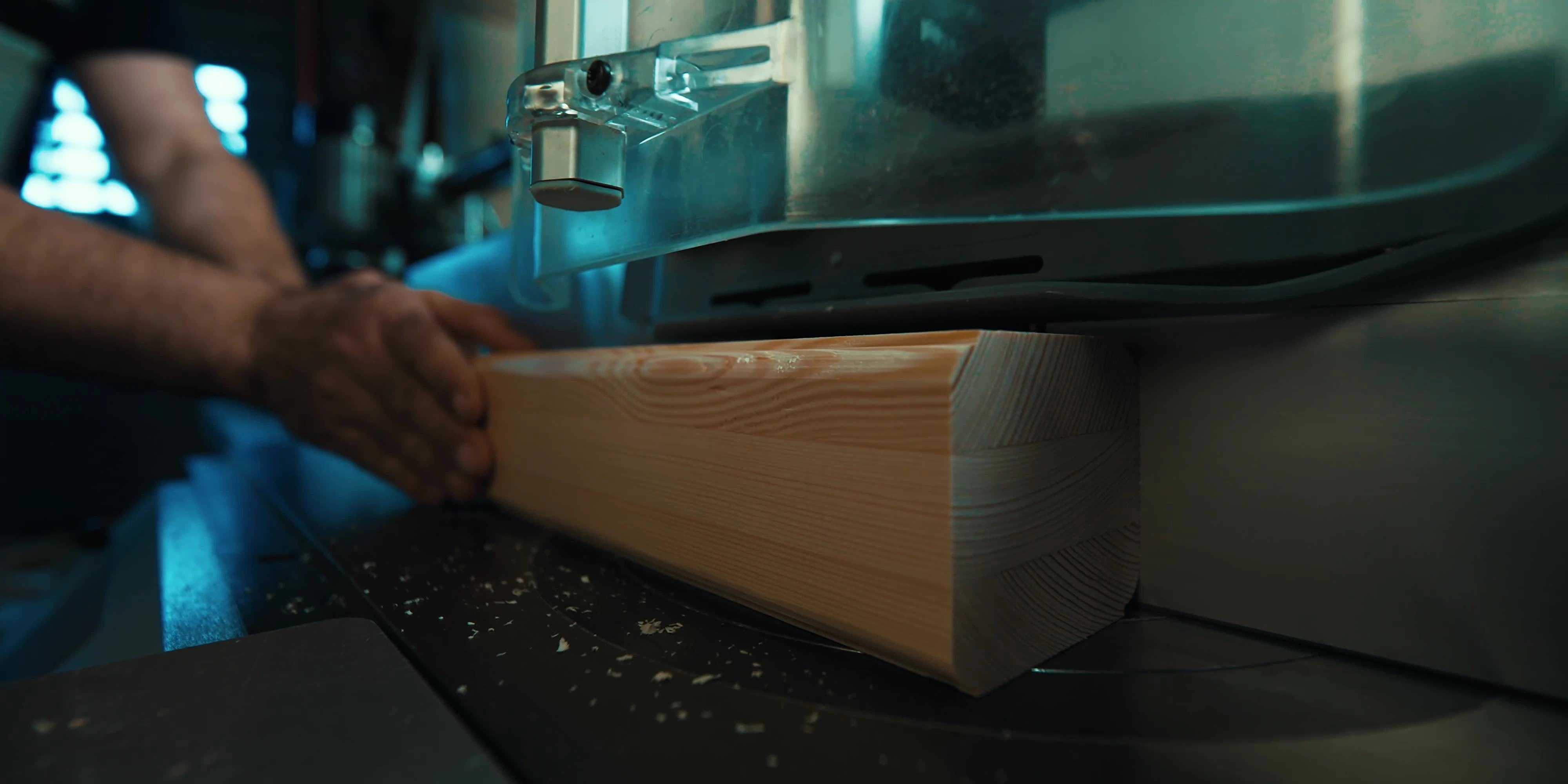 Hände eines Handwerkers, die ein Holzbauteil durch eine Holzbearbeitungsmaschine in einer Werkstatt führen.