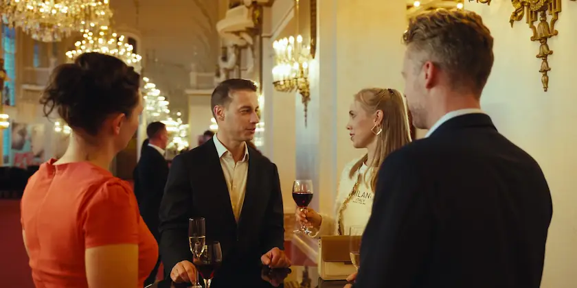 Elegante Gäste unterhalten sich bei Gläsern Wein in einem festlich beleuchteten Saal.
