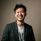 Portrait of a man smiling in gray sweater against dark background.