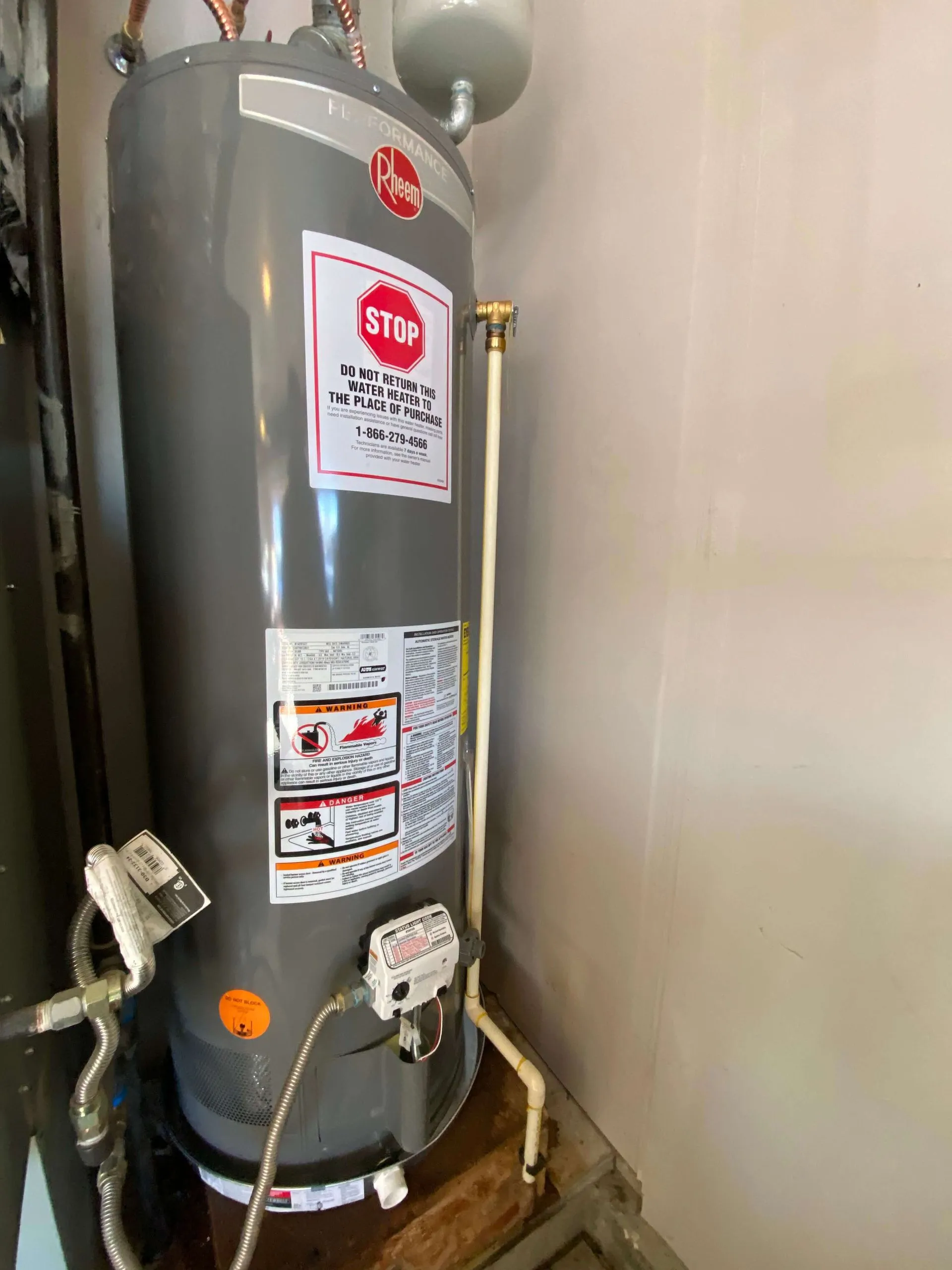 Gray Rheem water heater installed in a corner with warning and instruction labels attached.