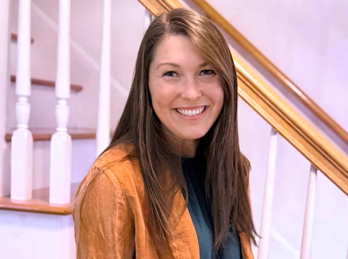 Real estate professional smiling in bright modern home with wooden staircase railing.