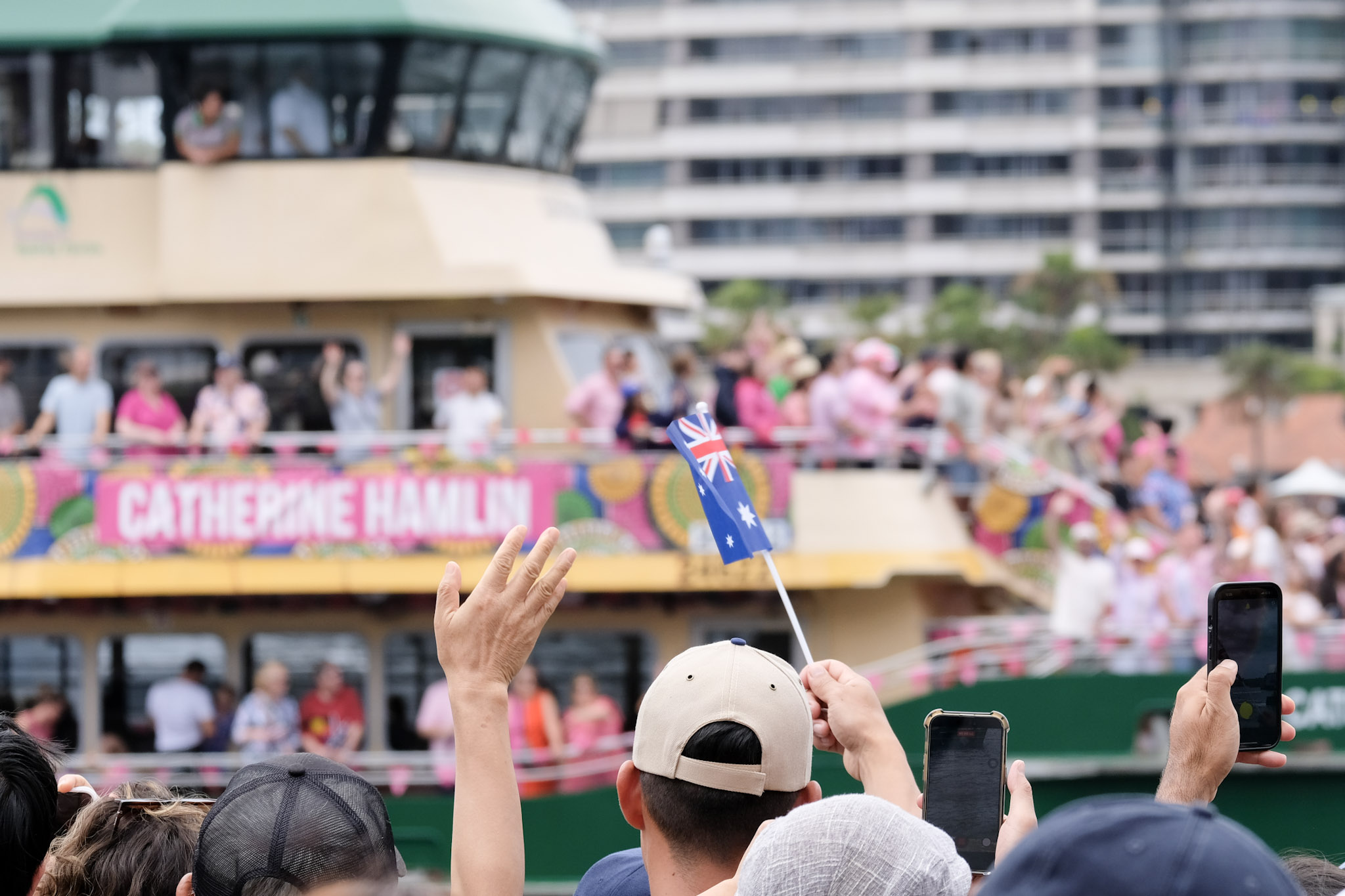 Crowd waving and taking photos of a ferry decorated with a Catherine Hamlin banner.