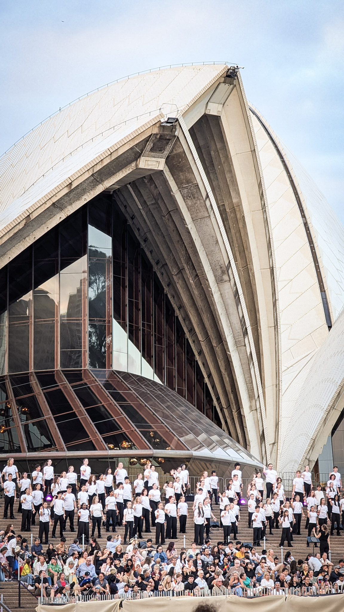 Large choir wearing performing on Sydney Opera House steps with an audience seated below.