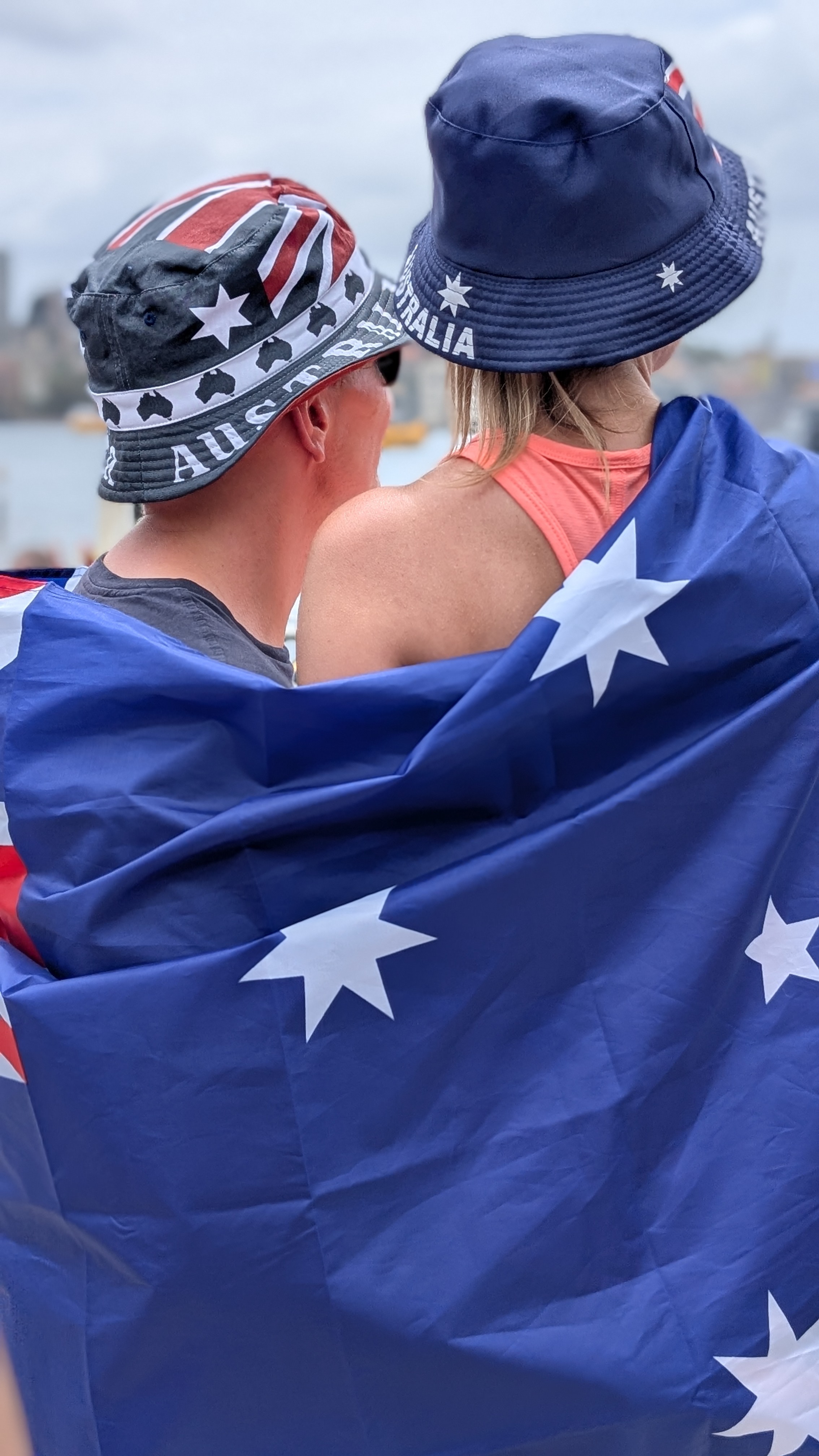 Couple wearing Australia-themed hats wrapped in an Australian flag, facing away from the camera.