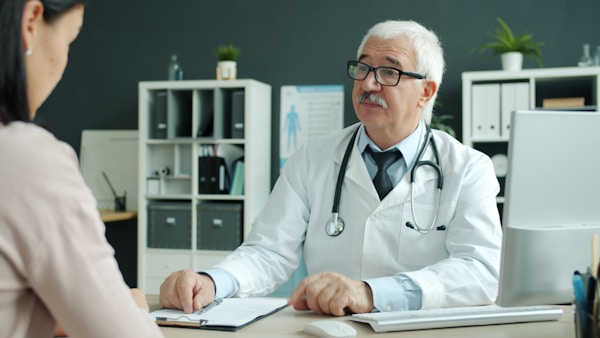 Male doctor and female patient are talking shaking hands during appointment in hospital sitting at desk in modern office. People and healthcare concept.