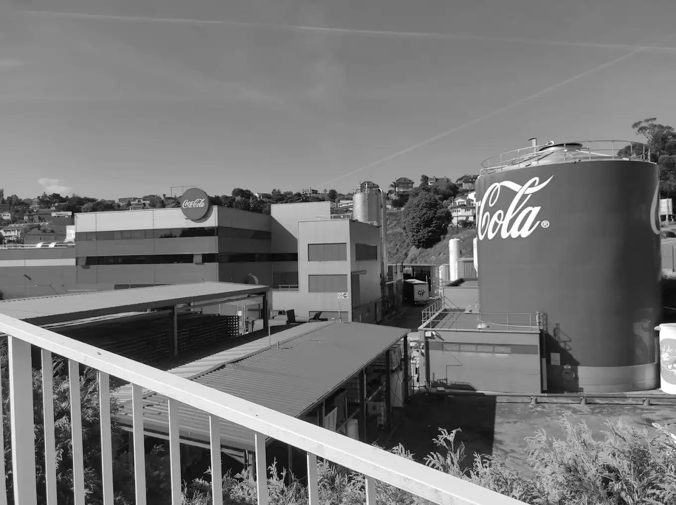 Coca-Cola manufacturing plant with large branded storage tanks and industrial buildings under a clear sky.