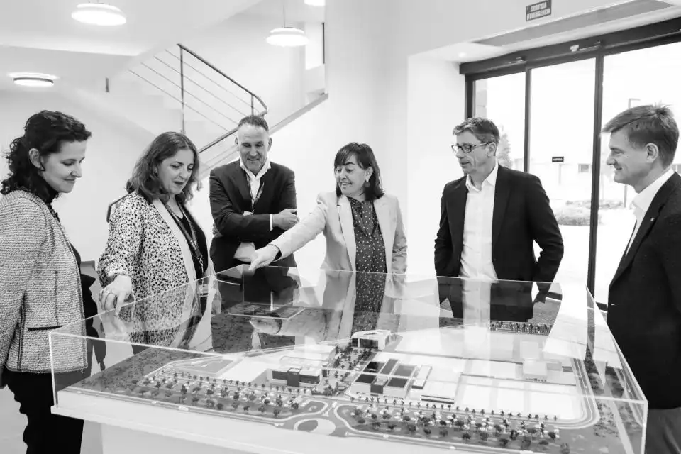 Six professionals standing around a large architectural model in a modern office space, engaged in discussion.