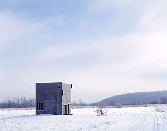 Simon Ungers' Cube House, a dark monolithic cube standing alone in a snow-covered field near Danby, New York.