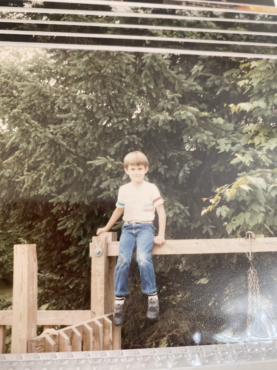 A boy standing on a wooden fence rail, photographed from a print still in its album sleeve, Kanawha County, about 1985.