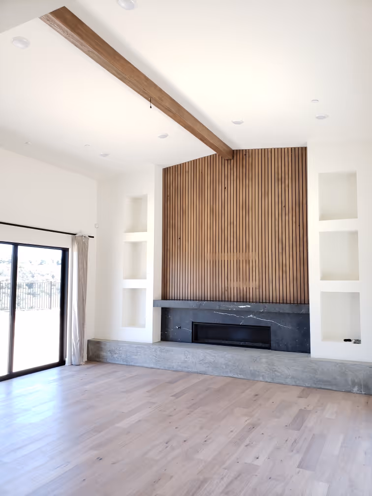 Modern living room with wood beam ceiling, large fireplace, and sliding glass doors, featuring light wood floors and built-in shelves