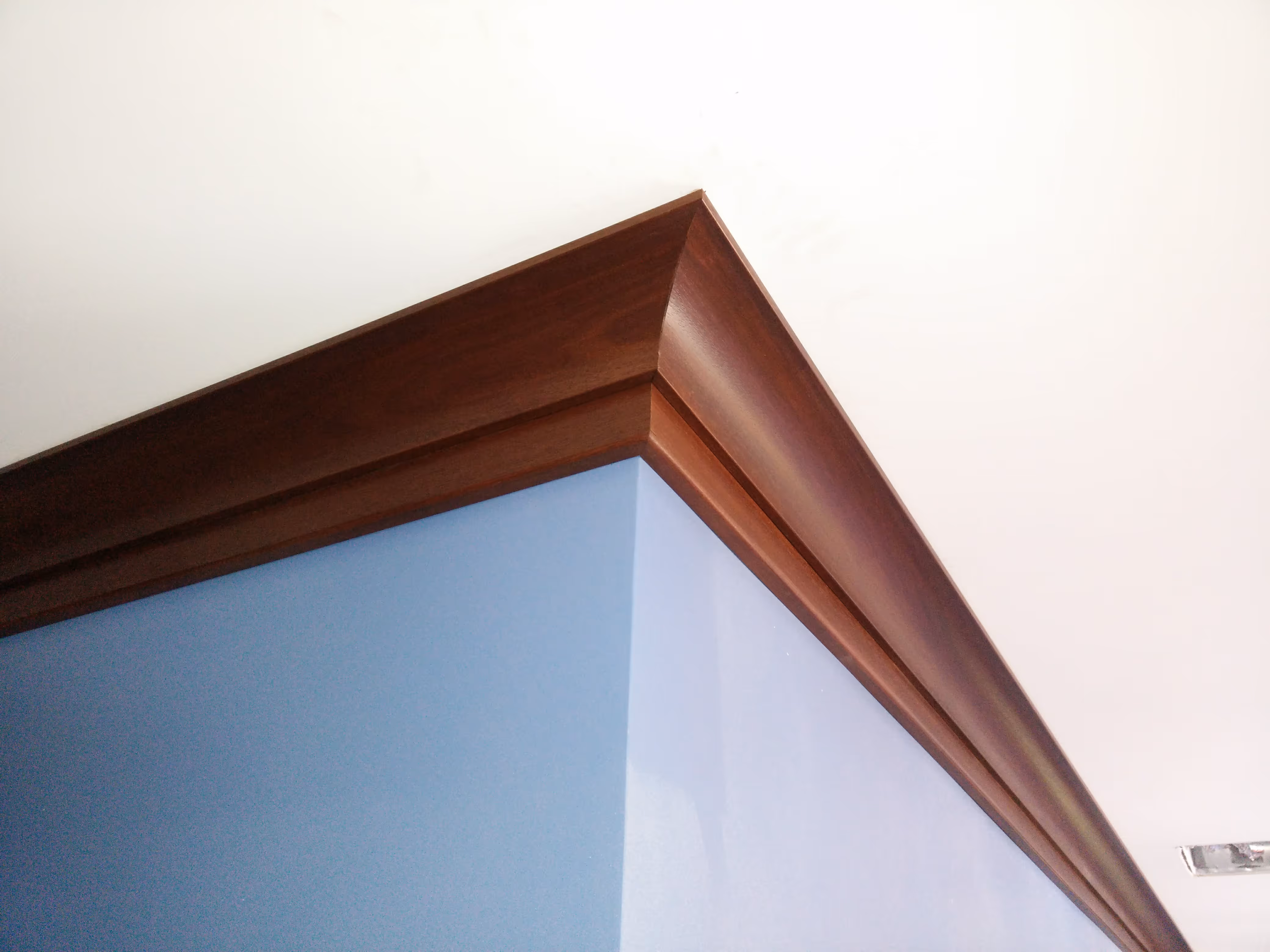 Wooden crown molding on a blue wall meets a white ceiling, highlighting the room's elegant architectural detail.