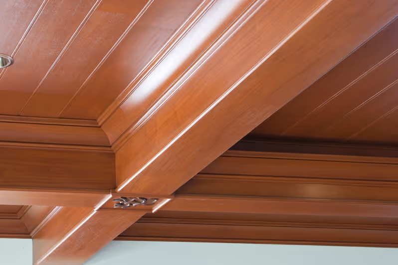 Rich wooden ceiling with intricate molding and warm tones, showcasing craftsmanship and elegant architectural detail.