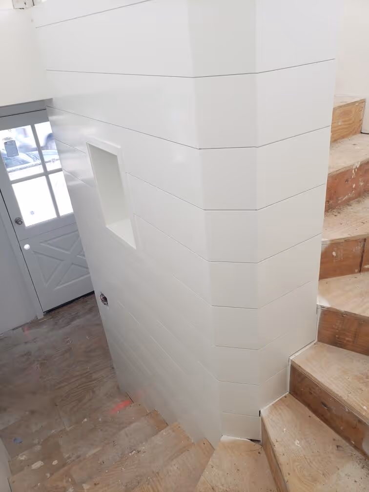 White shiplap accent wall wrapping around staircase newel post with built-in niche cutout, unfinished stairs visible
