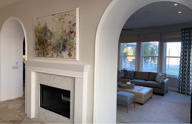 Arched doorway reveals a cozy living room with a gray sofa, large windows, and a fireplace adorned with abstract art.