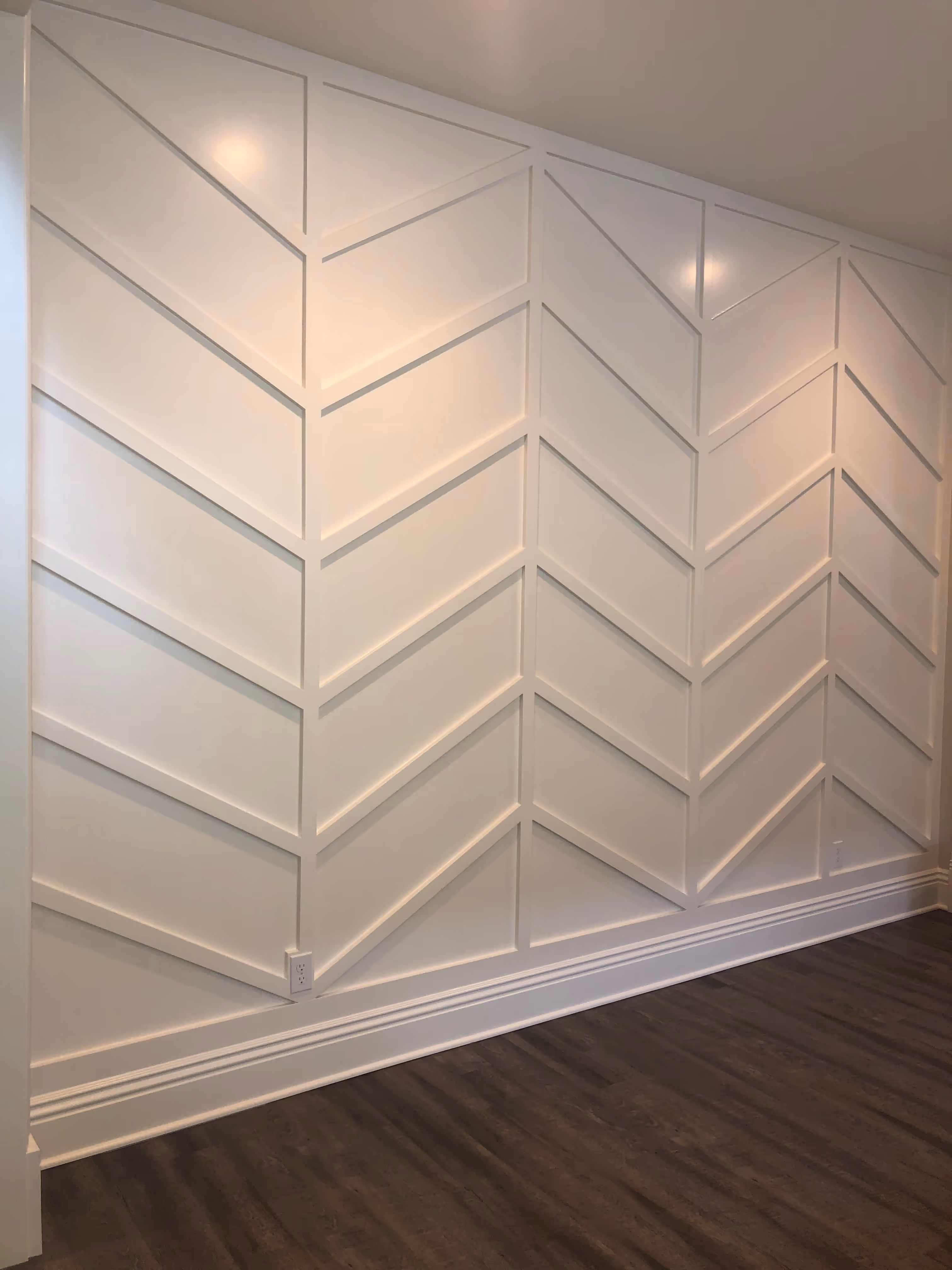 White wall with chevron pattern molding, contrasting dark wood floor, and soft lighting creates a modern, elegant interior design.