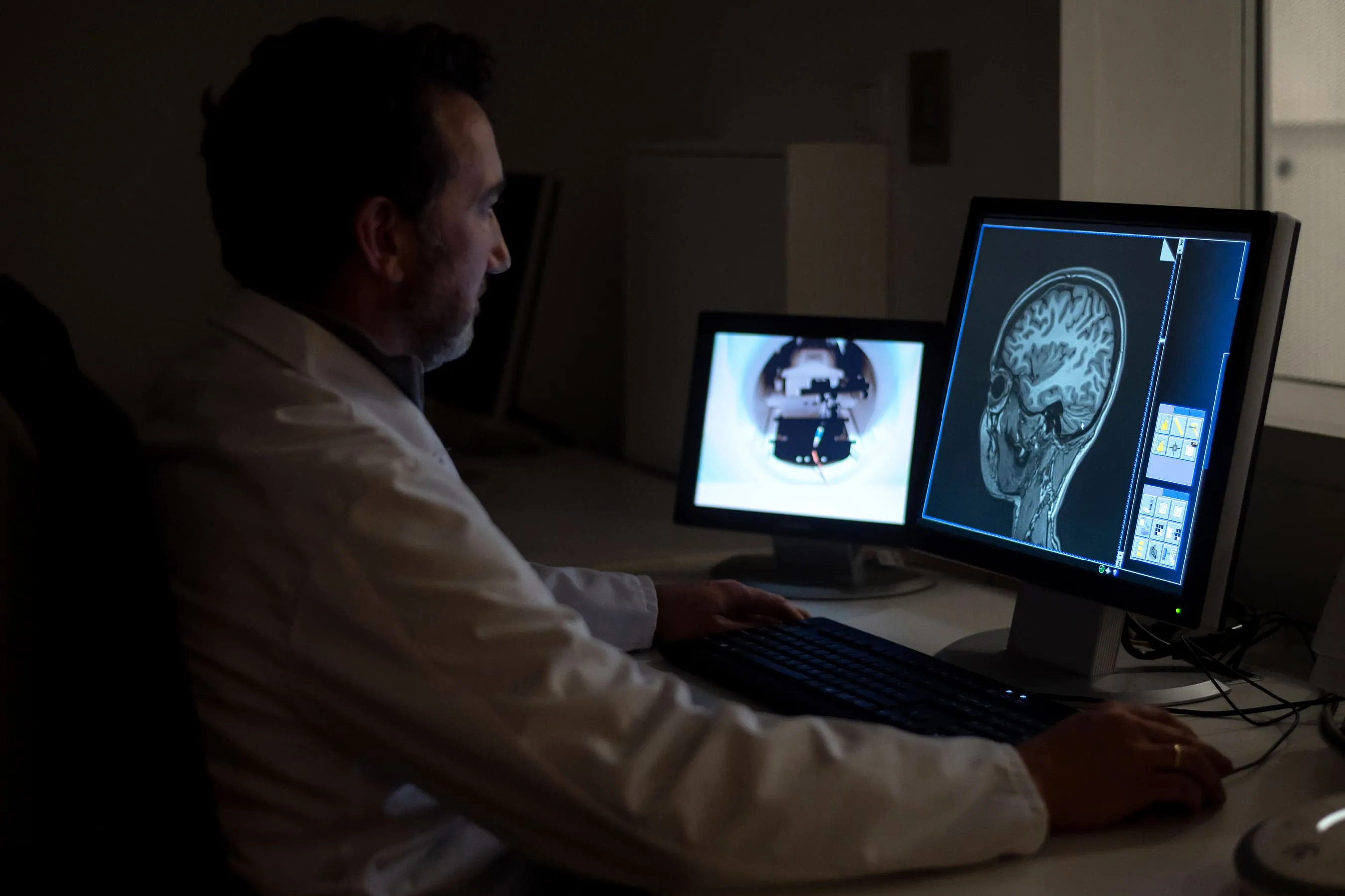 MRI technician sits in front of several monitors looking at scans