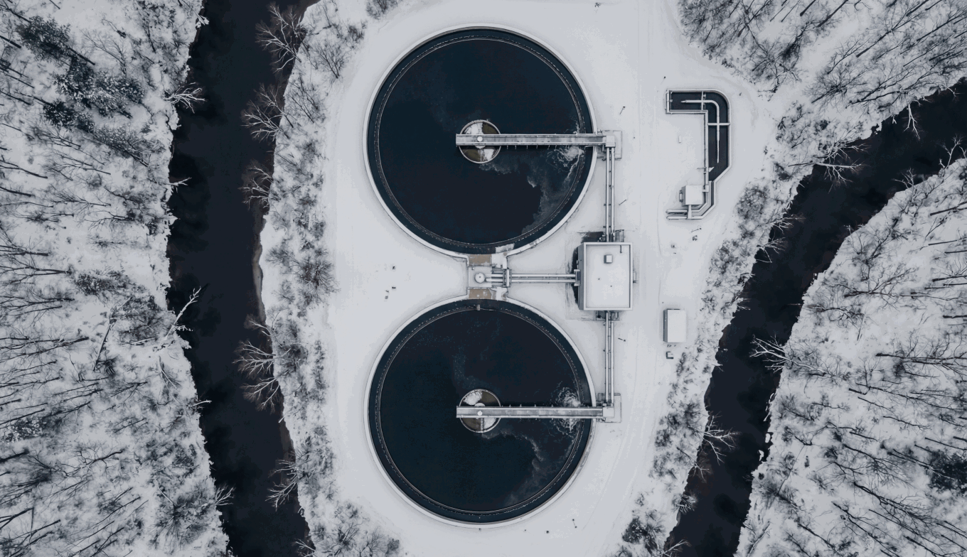 Aerial view of two circular water treatment tanks in a snowy forest landscape.