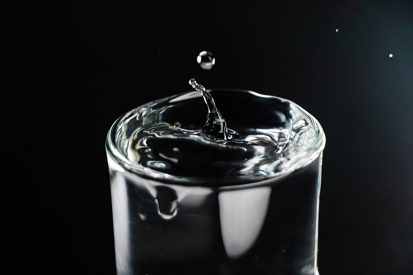 Close-up of a water droplet splashing into a glass filled to the brim against a black background.