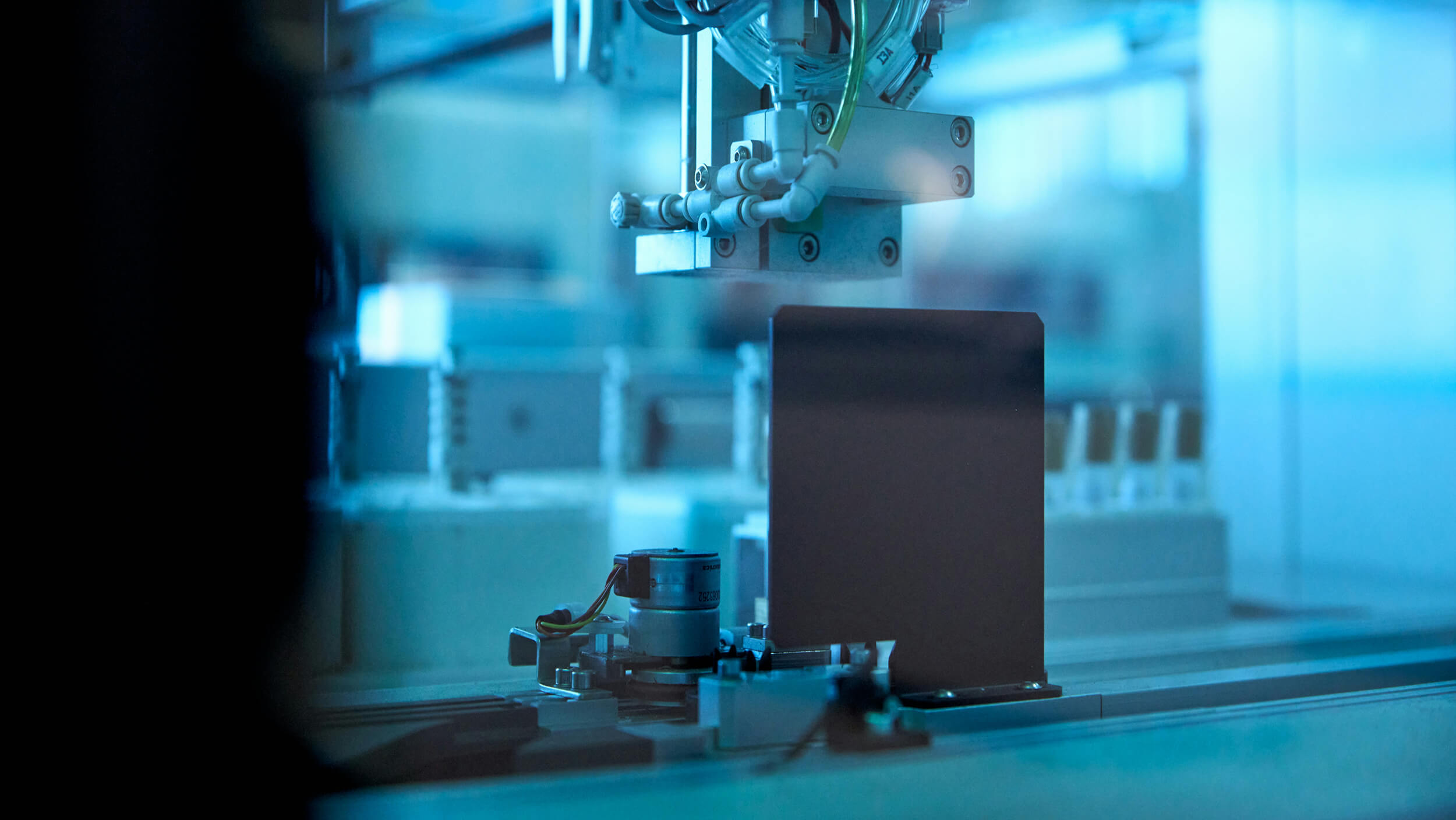 Close-up of automated industrial machinery with mechanical components and wiring under blue lighting.