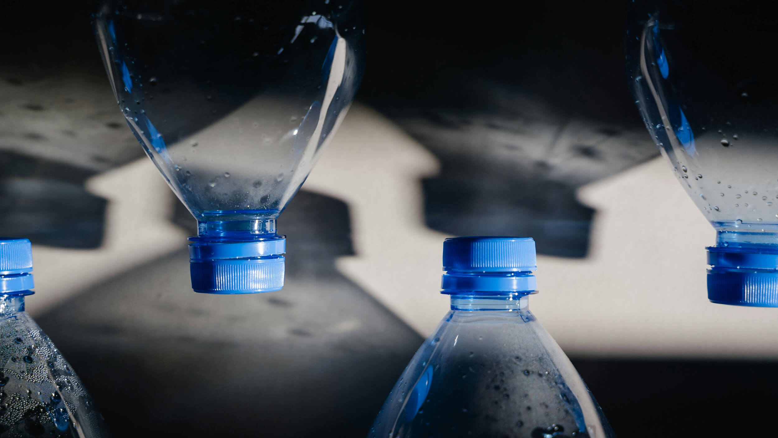 Close-up of water bottles with blue caps casting shadows on a surface.