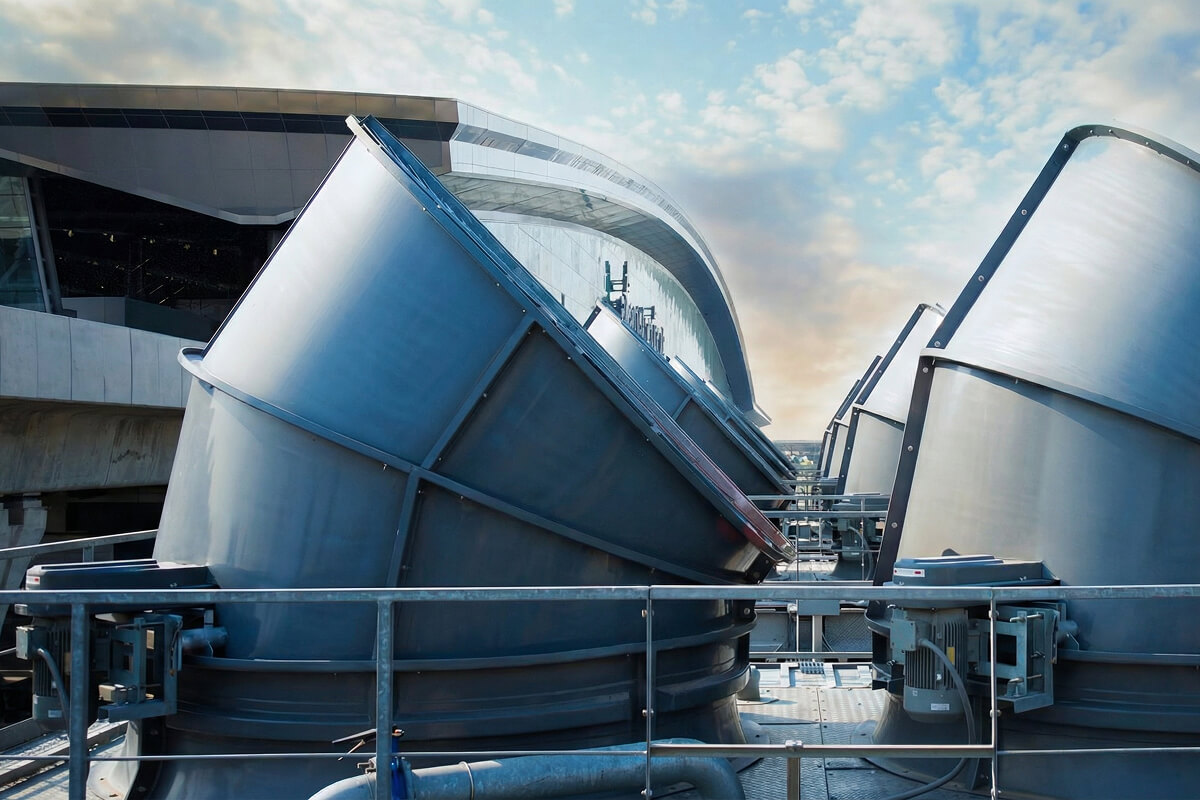 Row of large industrial metal ventilation ducts on rooftop under a partly cloudy sky.
