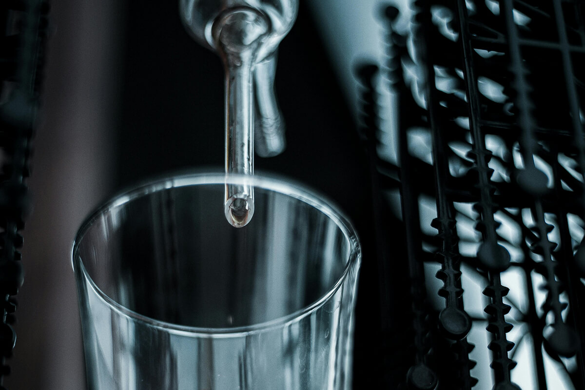 Close-up of a dropper releasing liquid into a clear glass container.