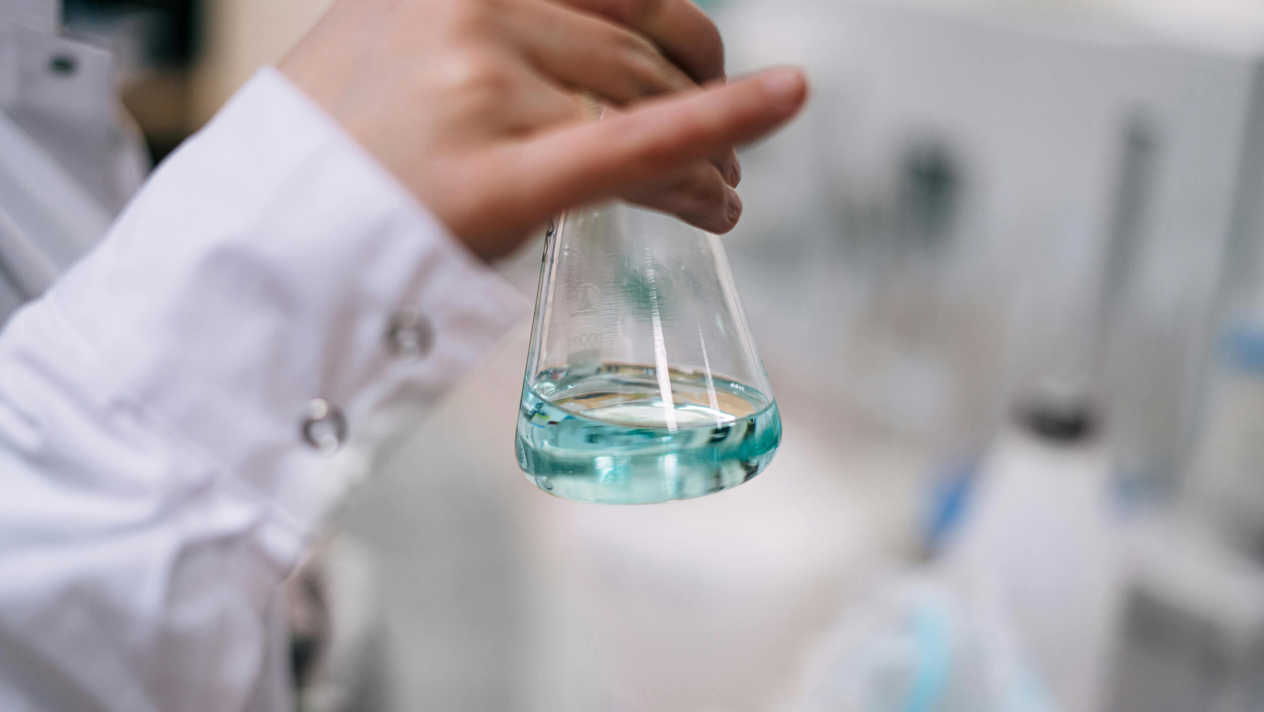 Hand holding a laboratory flask with light blue liquid inside.