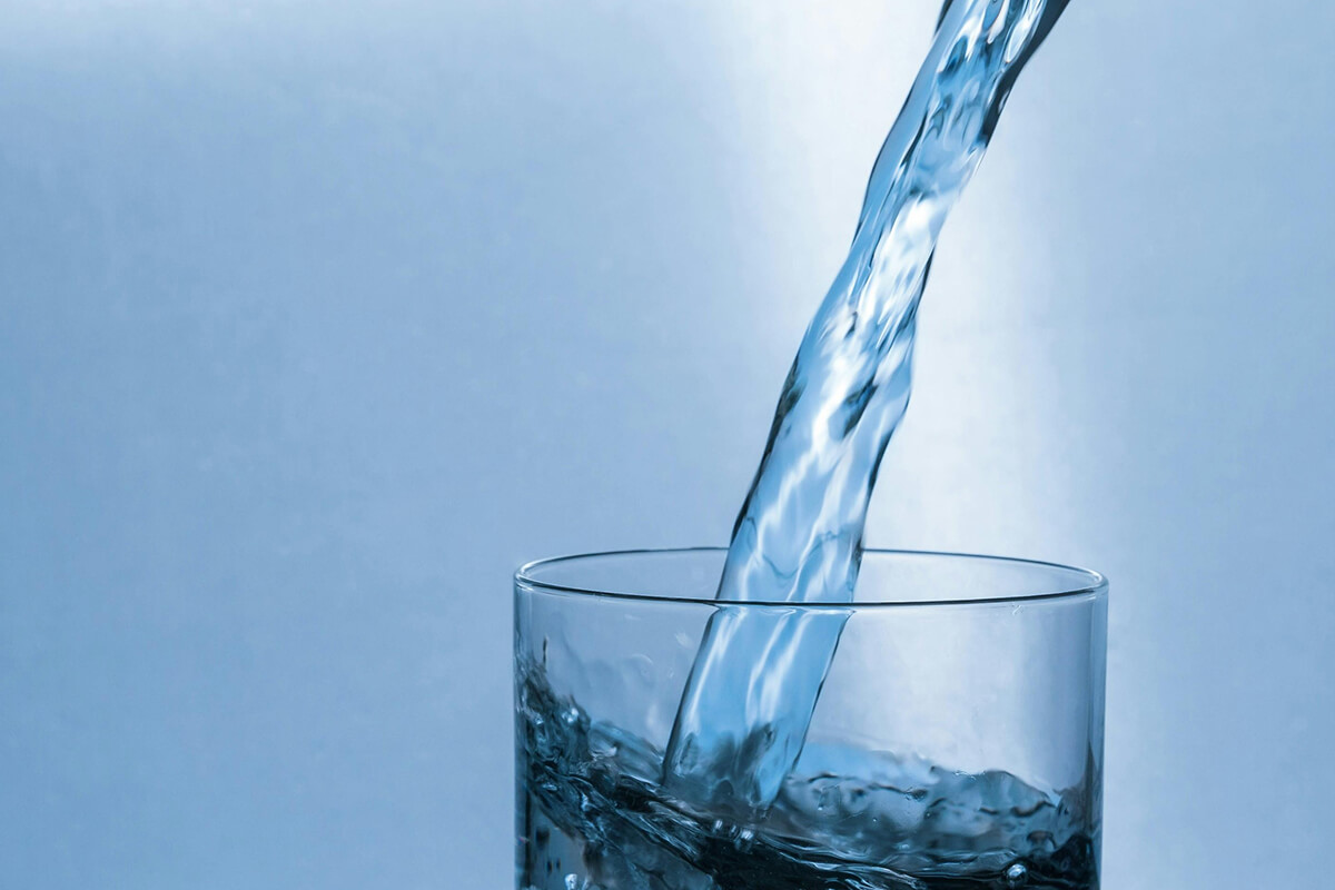 Clear water being poured into a transparent glass against a plain blue background.