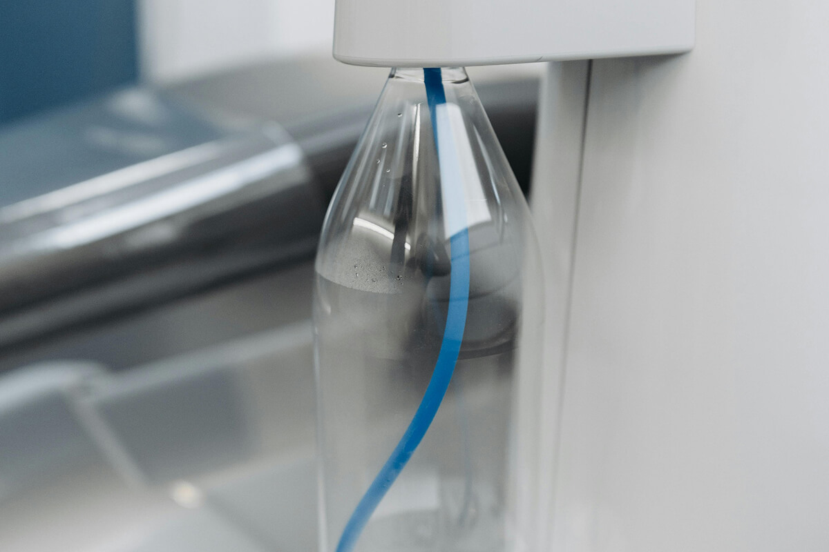 Close-up of a clear plastic bottle filling with water from a white dispenser with a blue tube inside.