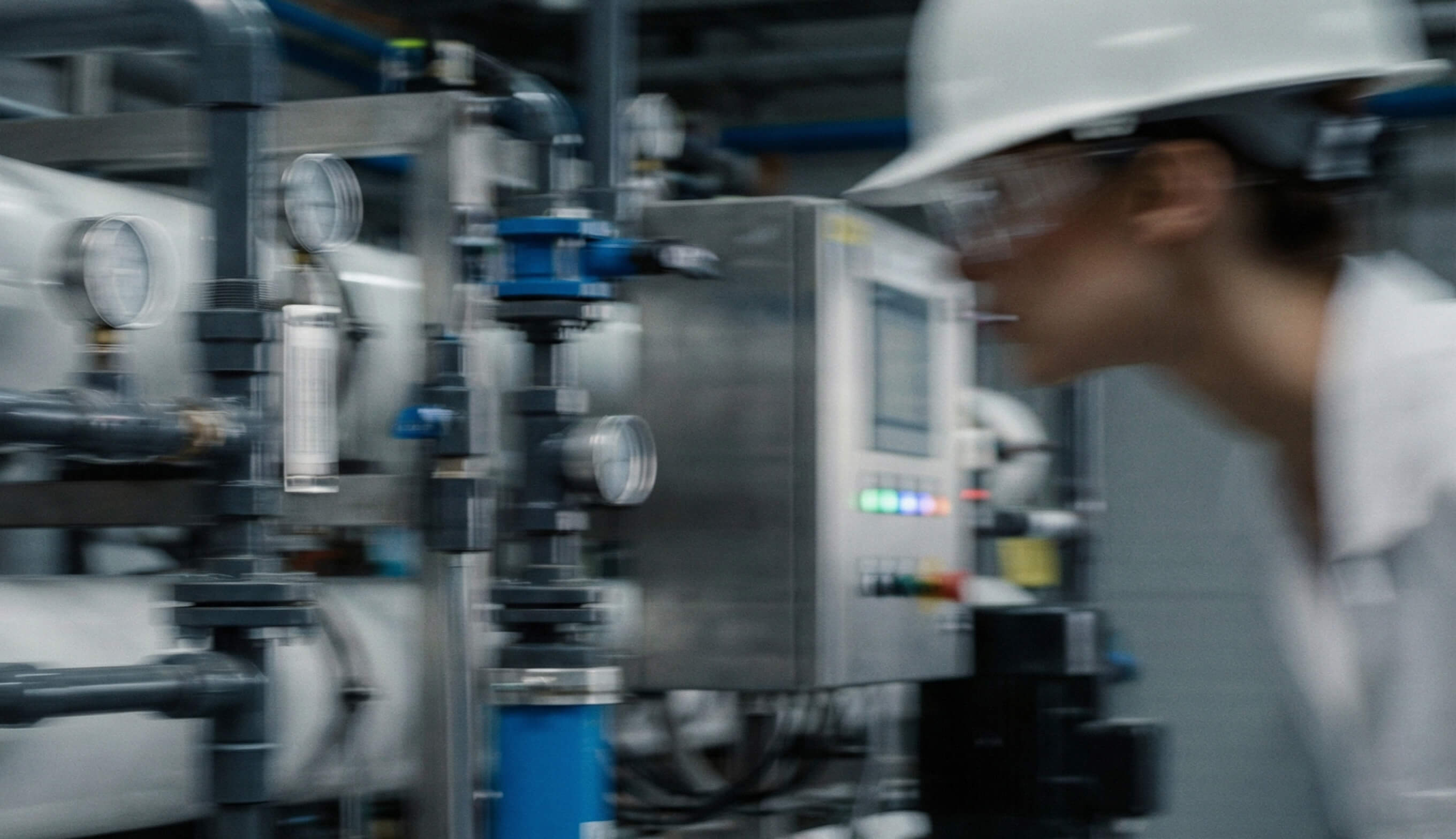 Engineer wearing a white hard hat inspecting industrial control panel and piping in a facility.
