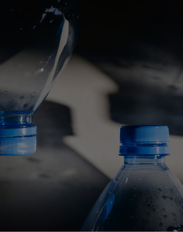 Two blue-capped plastic water bottles with water droplets against a dark background.