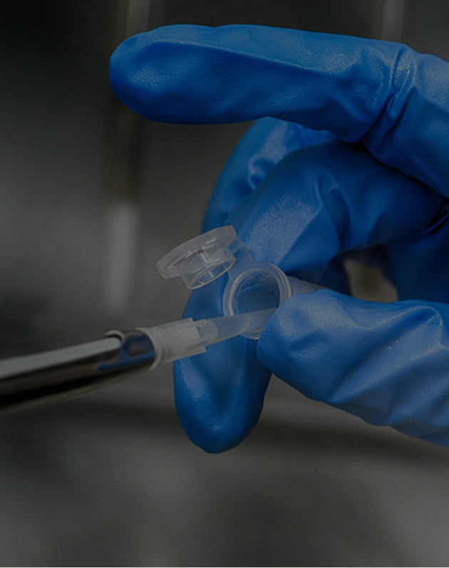 Gloved hand holding a small open plastic vial with a pipette inserting liquid inside.