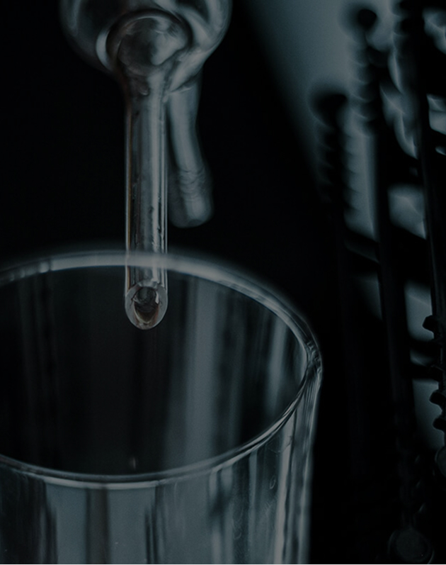 Close-up of a glass under a laboratory pipette with a drop of liquid about to fall.