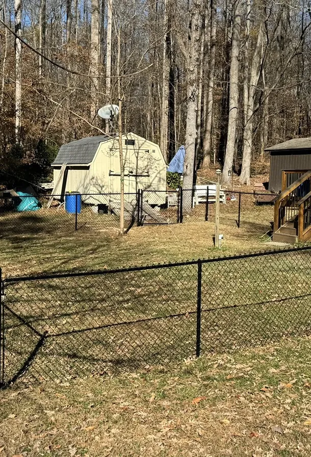Backyard with two sheds, chain-link fences, leafless trees, and a blue barrel under clear sky.